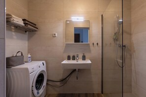 Ett litet badrum med tvättmaskin, handfat med spegel och en dusch med glasväggar.