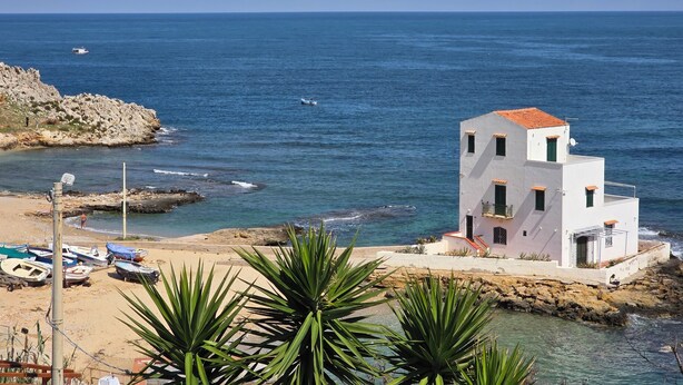 A coastal building with a red-tiled roof, situated on a rocky shore with clear blue sea in the background. - Marèa - Holiday House (Porticello)