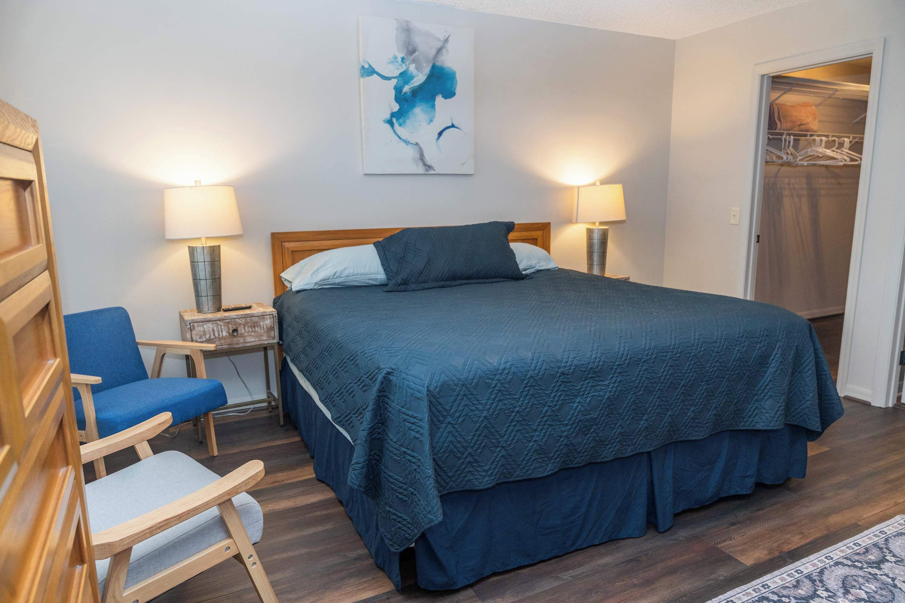 A bedroom with a bed, two bedside lamps, a chair, a small table, and a wardrobe.