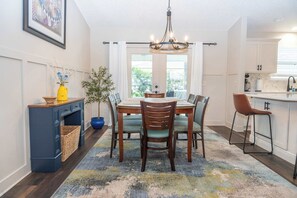 A dining area with a wooden table, chairs, a chandelier, and a view through large windows. - Heated Pool, Golf Cart, Life Stlye ID's (The Villages)