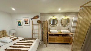 Ein Schlafzimmer mit einem Bett, einem Holzkopfstück, einem Nachttisch mit Lampe, einer Holzlade und einem Schminktisch mit zwei Waschbecken sowie einem Spiegel.
