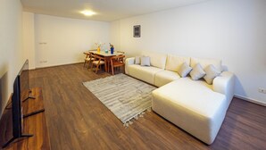 A living room with a wooden floor, a white sofa, a dining table with chairs, and a flat-screen TV. - Pharaohs Residence New Cairo El Rehab (New Cairo El rehab)