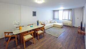 A modern living room with a dining area, featuring a wooden dining table, chairs, a sofa, and a TV stand. - Pharaohs Residence New Cairo El Rehab (New Cairo El rehab)
