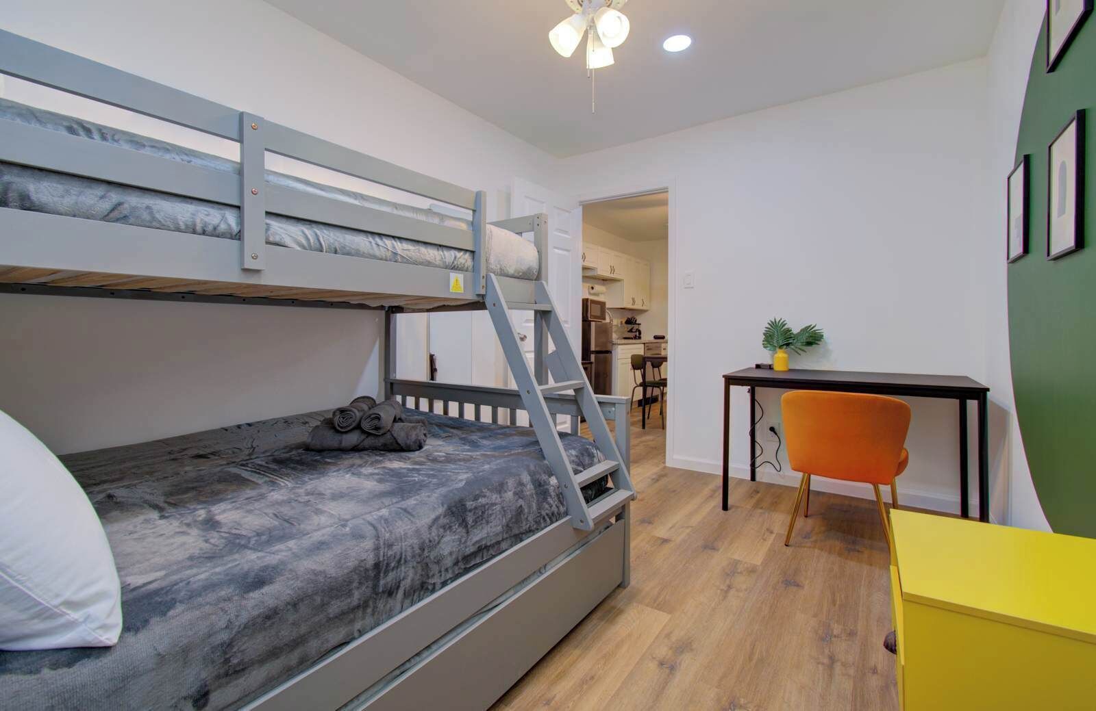 A bunk bed with a ladder, a desk with a chair, and a small table with a plant.