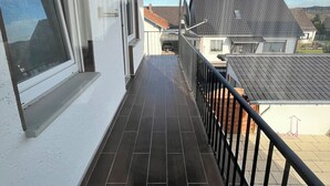 A balcony with a tiled floor, a window, and a railing.