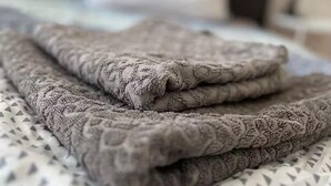 A neatly folded blanket on a bed with a patterned bedspread and a plain pillow.