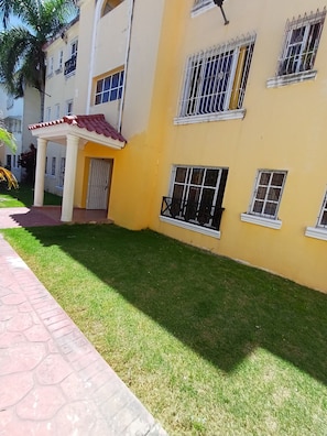 Un edificio amarillo con múltiples ventanas, un acceso cubierto y un césped bien cuidado.