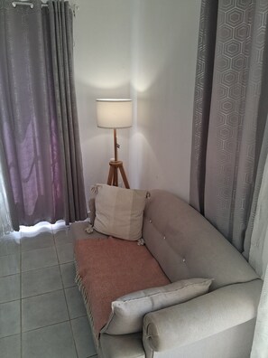 Eine Raumecke mit einer Couch, einer Lampe und gemusterten Vorhängen.