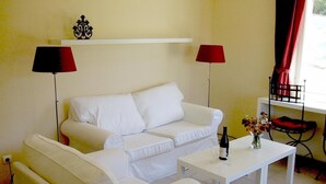 A white sofa and armchair set against a yellow wall, with a white table between them. A red lamp and a small decorative item are on the wall above the sofa. - A sunny living room with a loggia and a beautiful view of Mont Ventoux (Montbrun-les-Bains)