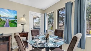 A dining area with a glass table, four chairs, a lamp, and a painting on the wall.