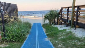 A pathway leading to a beach with a wooden boardwalk on the right and a fence on the left.