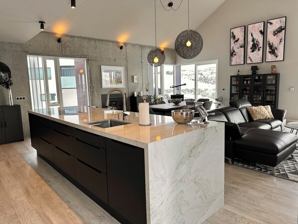 Une cuisine moderne dotée d’un grand îlot central, de meubles de rangement aux couleurs sombres et d’un éclairage suspendu.