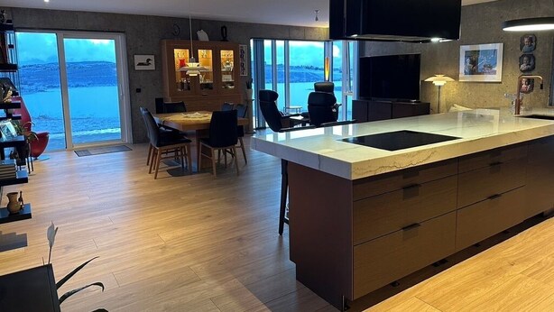 A modern kitchen with a large island, dining area with chairs, and a view of the sea. - Luxury lakefront Villa 15 min drive to downtown (Garðabær)