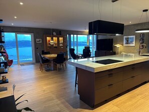 Une cuisine moderne dotée d’un grand îlot central, d’un coin repas avec des chaises et offrant une vue sur la mer.