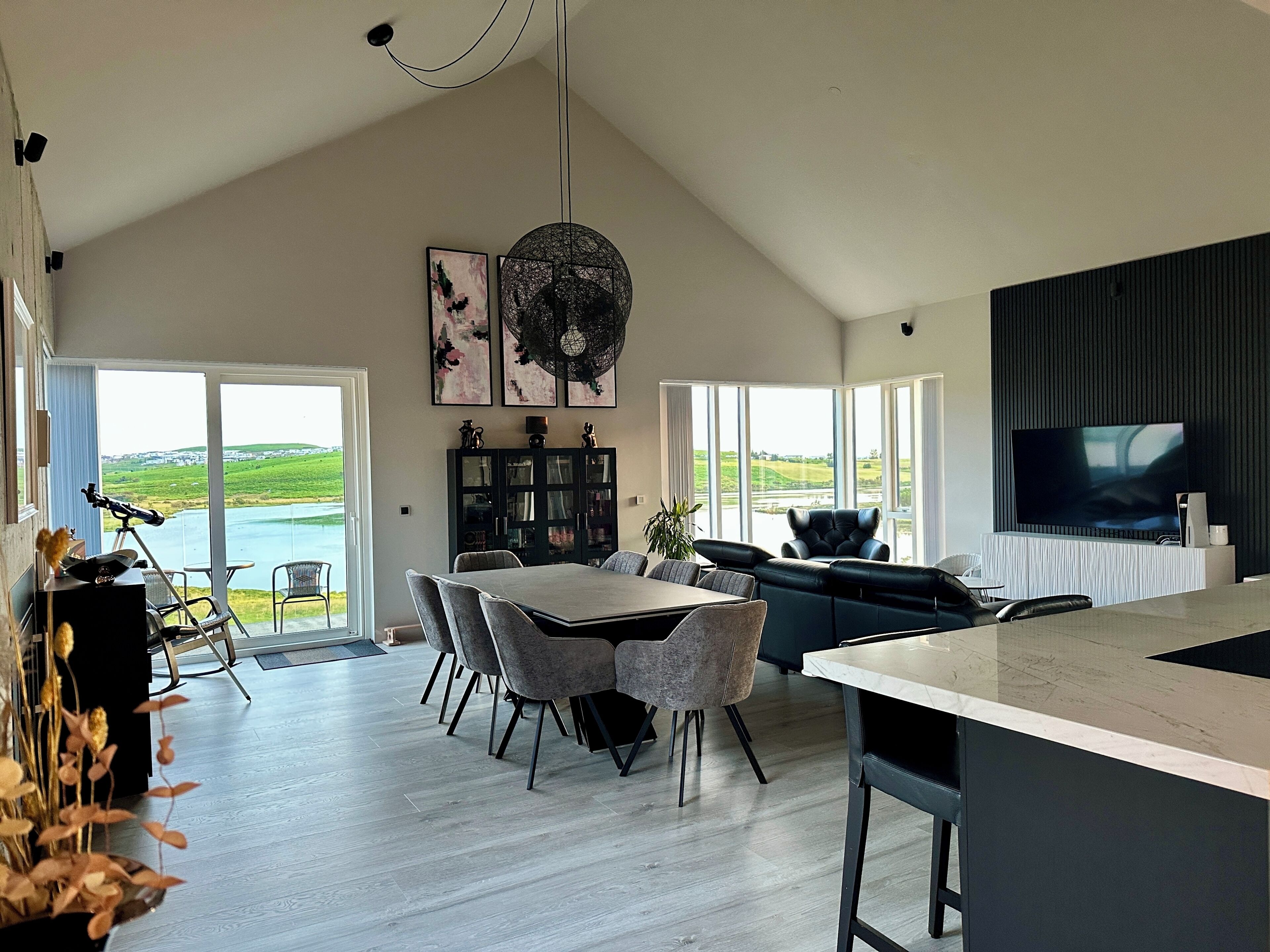 Une cuisine moderne dotée d’un grand îlot central, d’un coin repas avec des chaises et d’une vue sur un lac grâce à de grandes fenêtres.