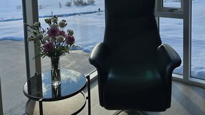 A room with a large window, a chair, and a small table with a vase of flowers. - Luxury lakefront Villa 15 min drive to downtown (Garðabær)