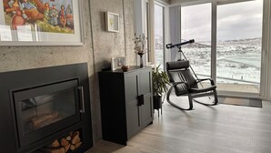 Una sala de estar moderna con chimenea, un ventanal con vistas nevadas, un sillón de cuero negro y un cuadro en la pared.