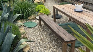 A patio area with a wooden table and benches, surrounded by a wooden fence and various plants.
