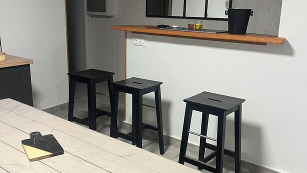 A dining area with a wooden table, four black stools, and a wooden shelf above the table.