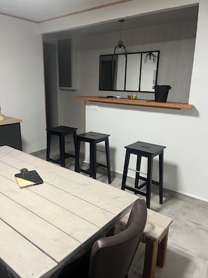 Un comedor con una mesa de madera, cuatro taburetes negros y un estante de madera sobre la mesa.