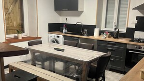 A compact kitchen with a dining area, a washing machine, and a window with wooden shutters.