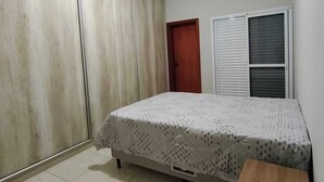 A bedroom with a bed, wardrobe, and a small cabinet. - CASA FLORENÇA (Indaiatuba)