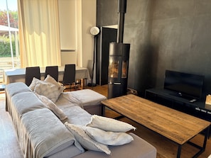 A modern living room with a sofa, a wooden coffee table, a TV, and a black wood-burning stove. - Courtoin Mill Guesthouse (Vimory)
