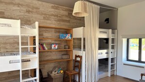 Une chambre avec des lits superposés, une bibliothèque, un fauteuil en osier et une fenêtre donnant sur un beau paysage.