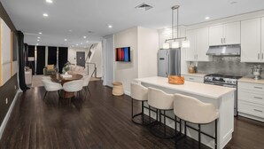Une cuisine moderne avec des meubles blancs, un réfrigérateur en acier inoxydable et un îlot central doté de tabourets de bar.