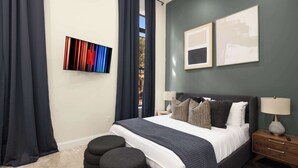 Une chambre à coucher avec un lit, des tables de chevet, une télévision et une fenêtre avec des rideaux.