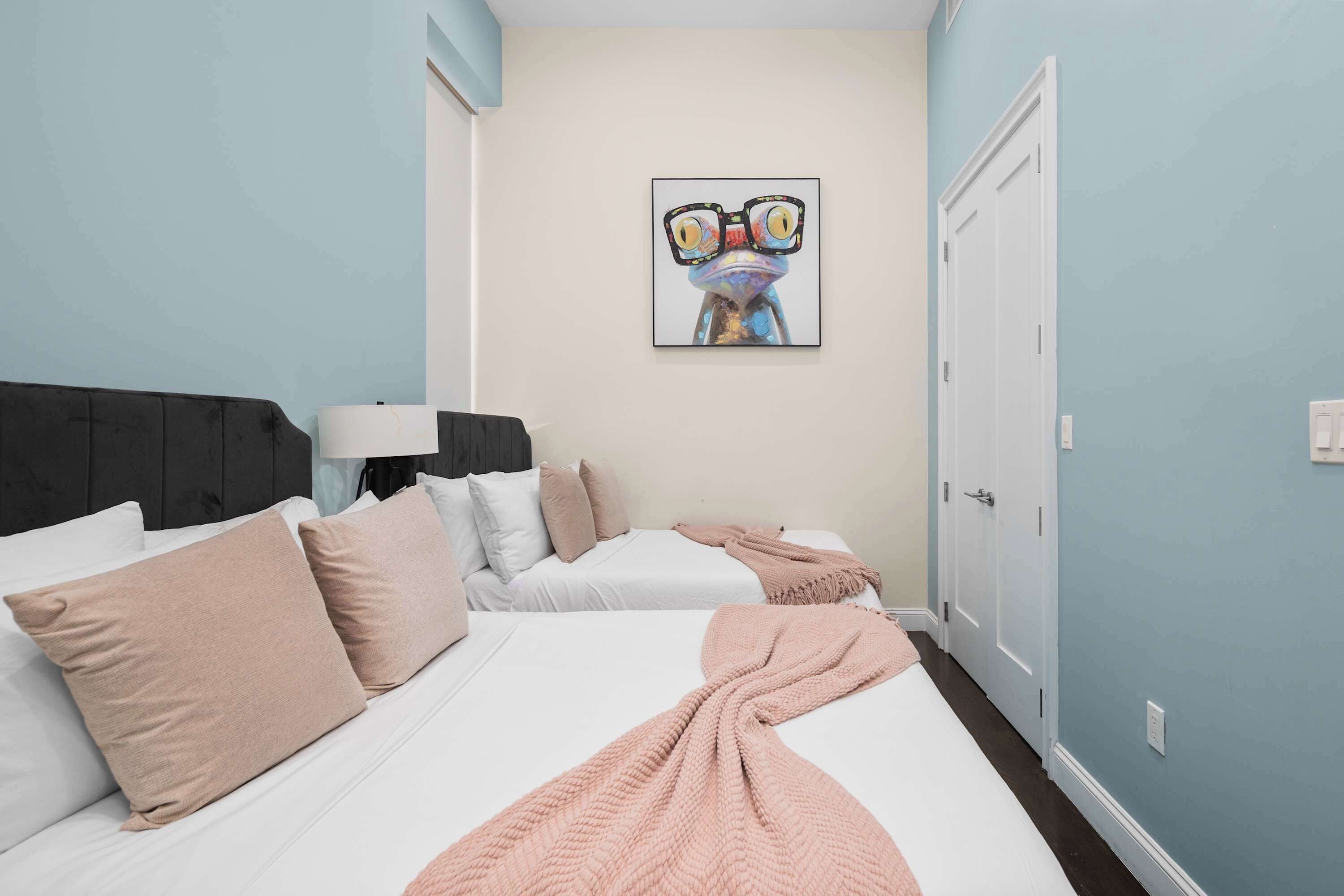 Een hotelkamer met twee bedden, een groot schilderij aan de muur en een deur aan de rechterkant.
