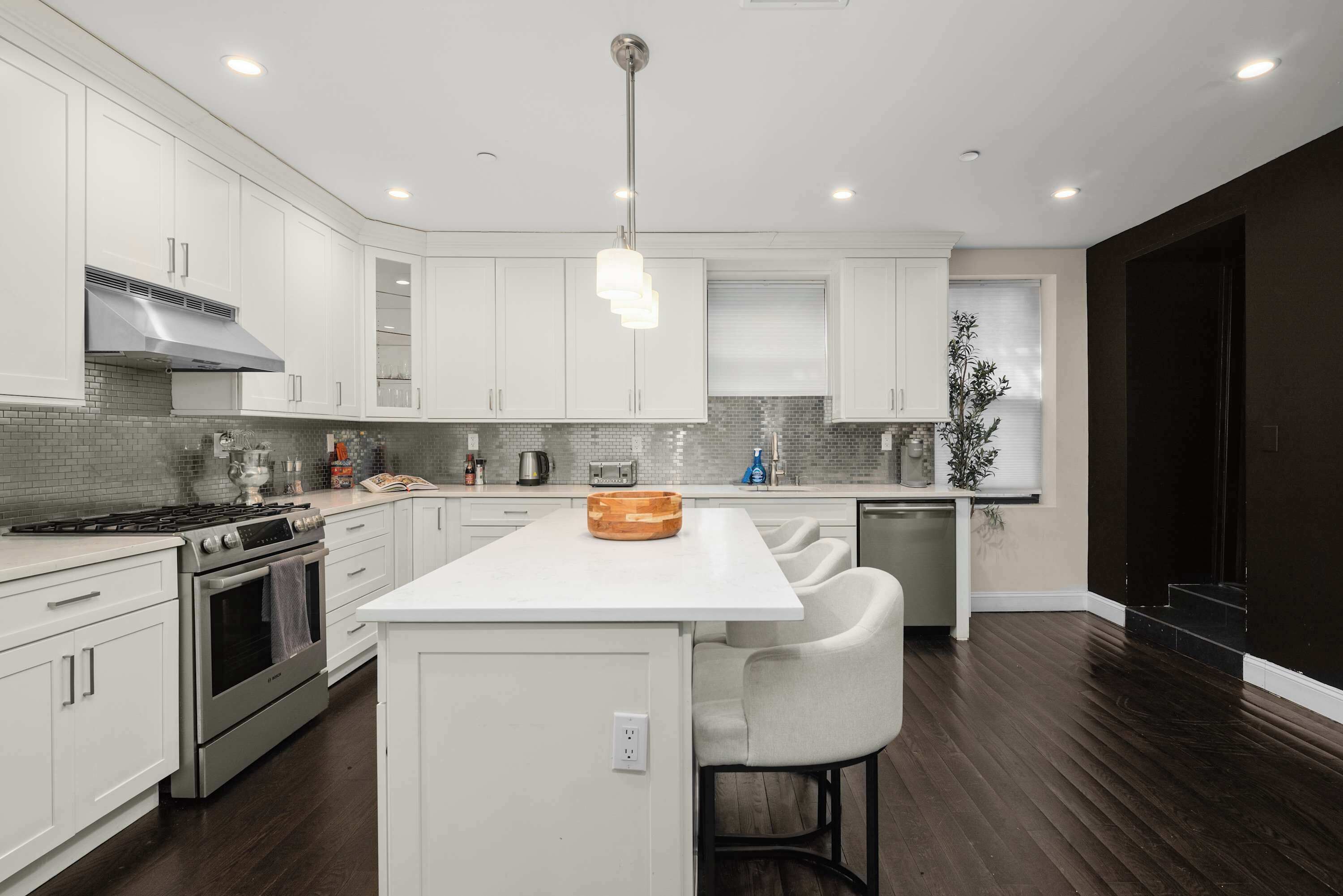A modern kitchen with white cabinetry, a central island, stainless steel appliances, and a dark wood floor.