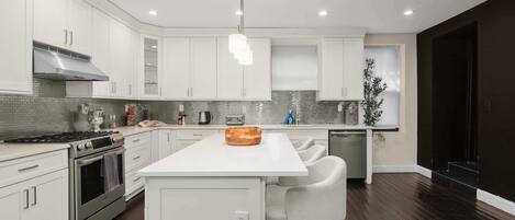 A modern kitchen with white cabinetry, a central island, stainless steel appliances, and a dark wood floor.
