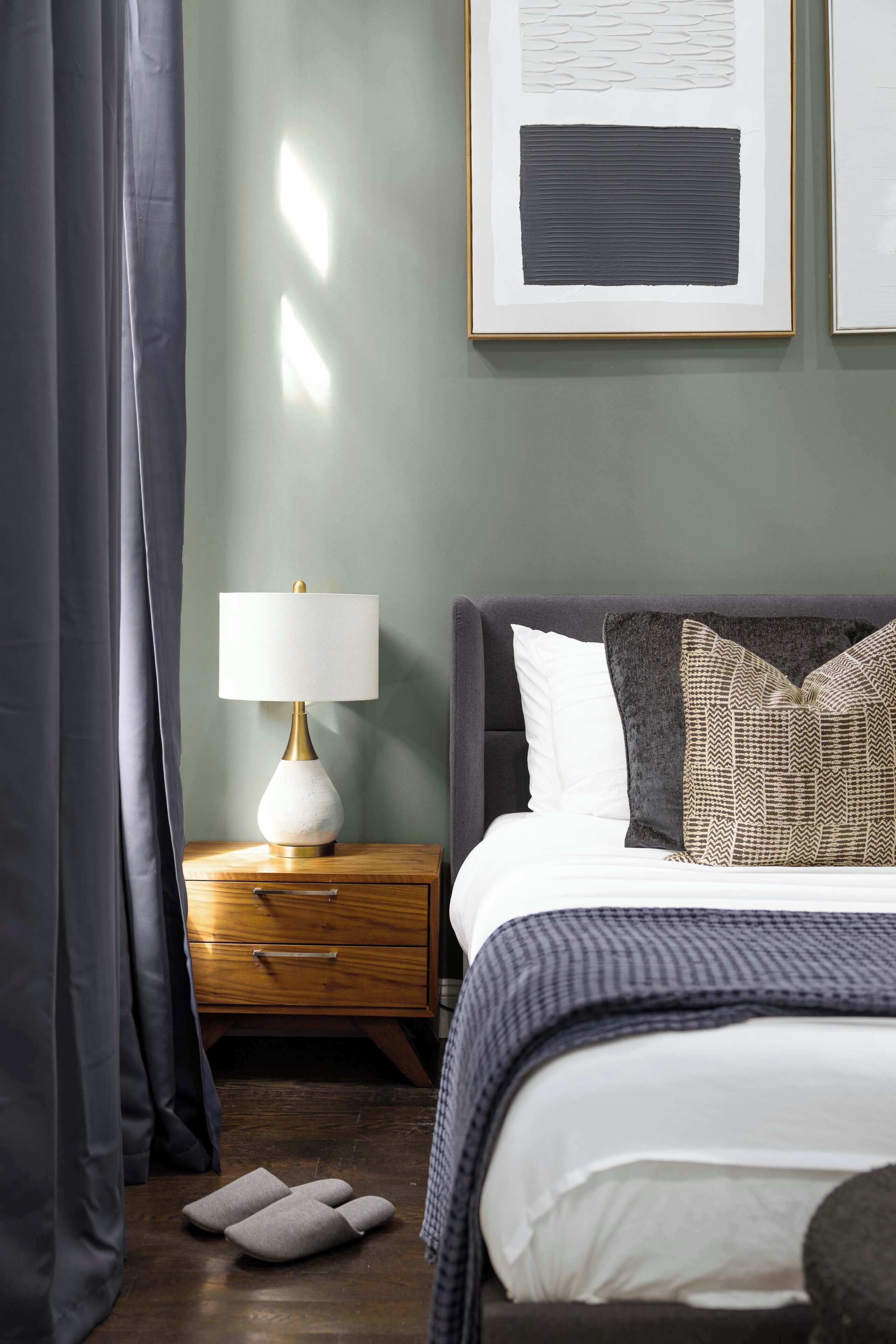 A neatly made bed with pillows, a bedside lamp, a wooden nightstand, and a framed picture on the wall.
