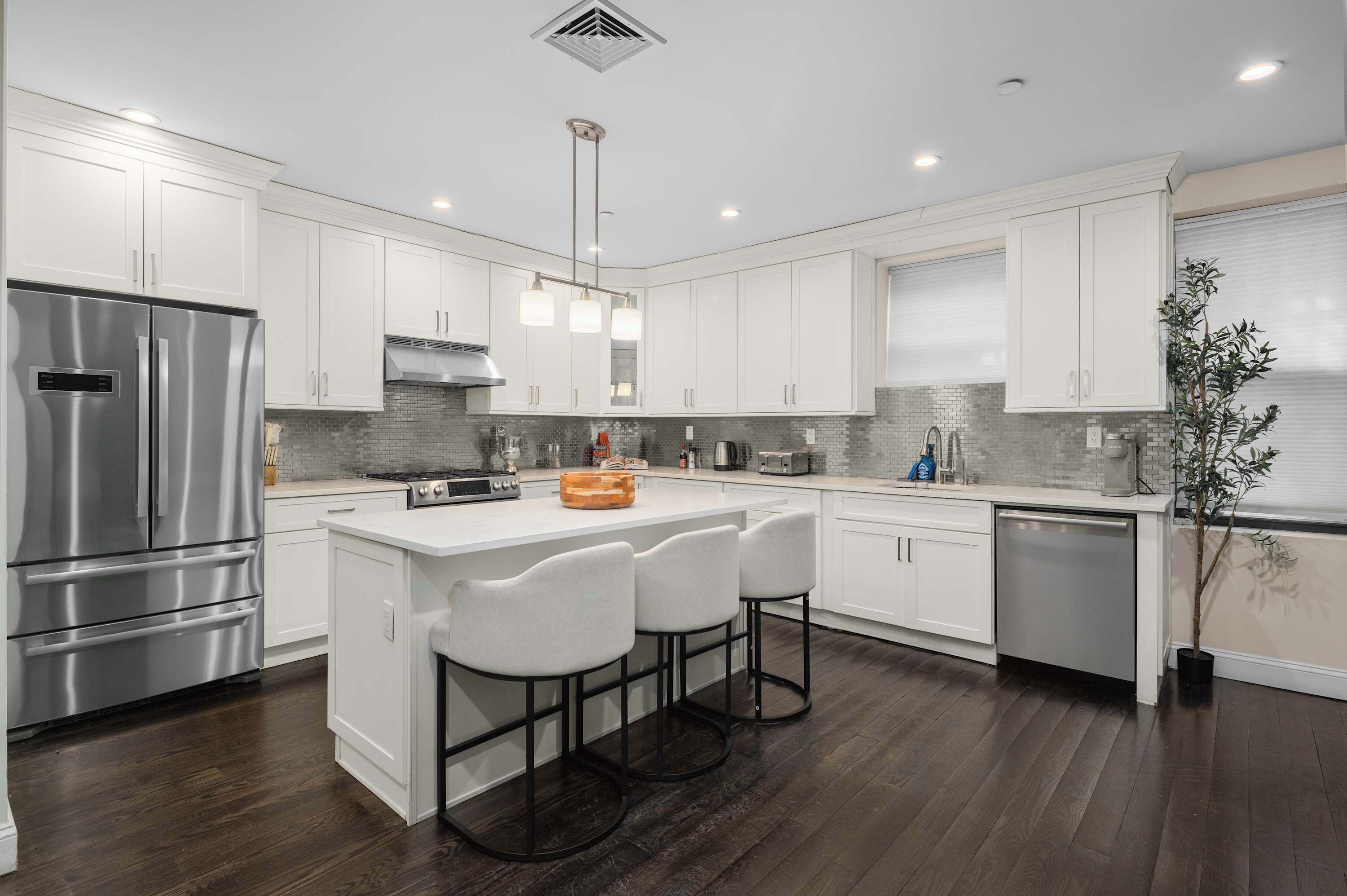A modern kitchen with white cabinets, stainless steel appliances, a central island with bar stools, and a potted plant.