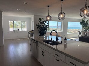 A modern kitchen with a large island, pendant lighting, and a view of the outdoors.