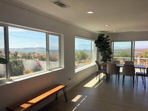 A spacious room with large windows, a wooden bench, and a dining area with chairs and a table.