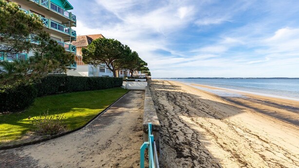 A beachfront property with a paved walkway leading to the beach, a grassy area, and a building with balconies. - Emerald apartment with beach access in Pereire (Arcachon)