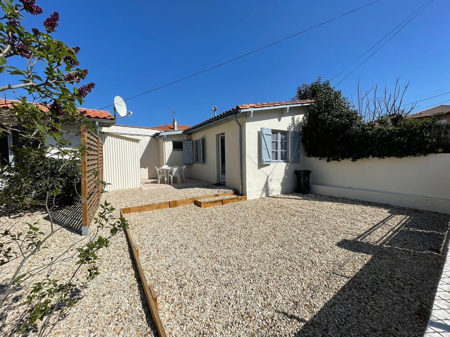 A small, single-story house with a gravel patio, a wooden deck, and a satellite dish.