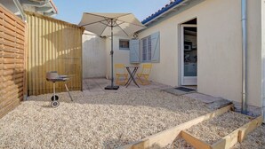 Een klein terras buiten met een houten tafel en stoelen, een barbecue en een parasol.