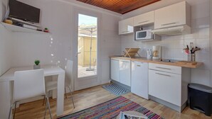Een kleine keuken met witte kastjes, een magnetron en een eethoekje met een witte tafel en stoel.