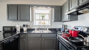 Una cocina con armarios gris oscuro, encimera negra, campana extractora de acero inoxidable, microondas, fregadero y ventana decorada con una bicicleta.