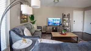 A living room with a grey sofa, a coffee table, a TV, and a bookshelf. - Ridge Retreats Unit B - Balcony/Wifi/4 Queen Beds (Birmingham)
