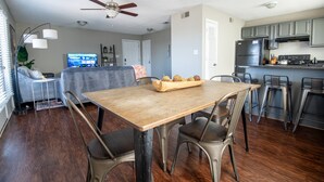 A modern kitchen with stainless steel appliances, a dining area with a wooden table and metal chairs, and a living area with a sofa and TV. - Ridge Retreats Unit B - Balcony/Wifi/4 Queen Beds (Birmingham)