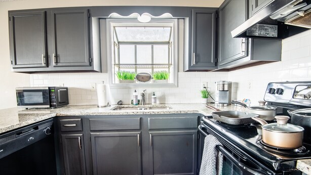 Une cuisine avec des meubles de couleur sombre, un four à micro-ondes, une cuisinière et une fenêtre donnant sur un paysage verdoyant.