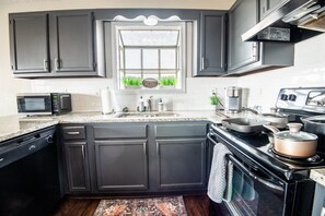 A kitchen with dark cabinets, a microwave, a stove, and a window with a view of greenery.