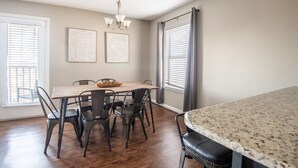 Un coin repas avec une table et des chaises en bois, un lustre et des œuvres d’art accrochées aux murs.
