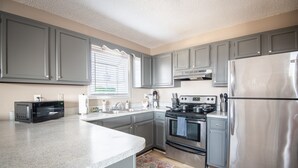 A kitchen with grey cabinets, a stainless steel refrigerator, a microwave, and a stove. - Ridge Retreats Unit E- WiFi/4 Queen Beds/Groups (Birmingham)