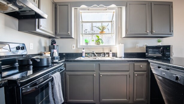 A kitchen with grey cabinets, a black stove, a microwave, and a window with plants. - Ridge Retreats - Unit F: King Bed/Free Parking/TVs (Birmingham)