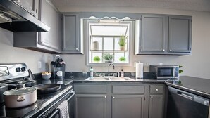 A kitchen with grey cabinets, a black countertop, a stove, a sink, a microwave, and a window with plants. - Ridge Retreats Duo: Big Groups/Free Parking/Wifi (Birmingham)